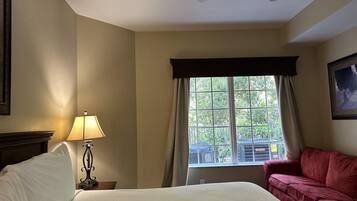 A hotel room with a bed, a red sofa, a window with curtains, a lamp, and a ceiling fan.