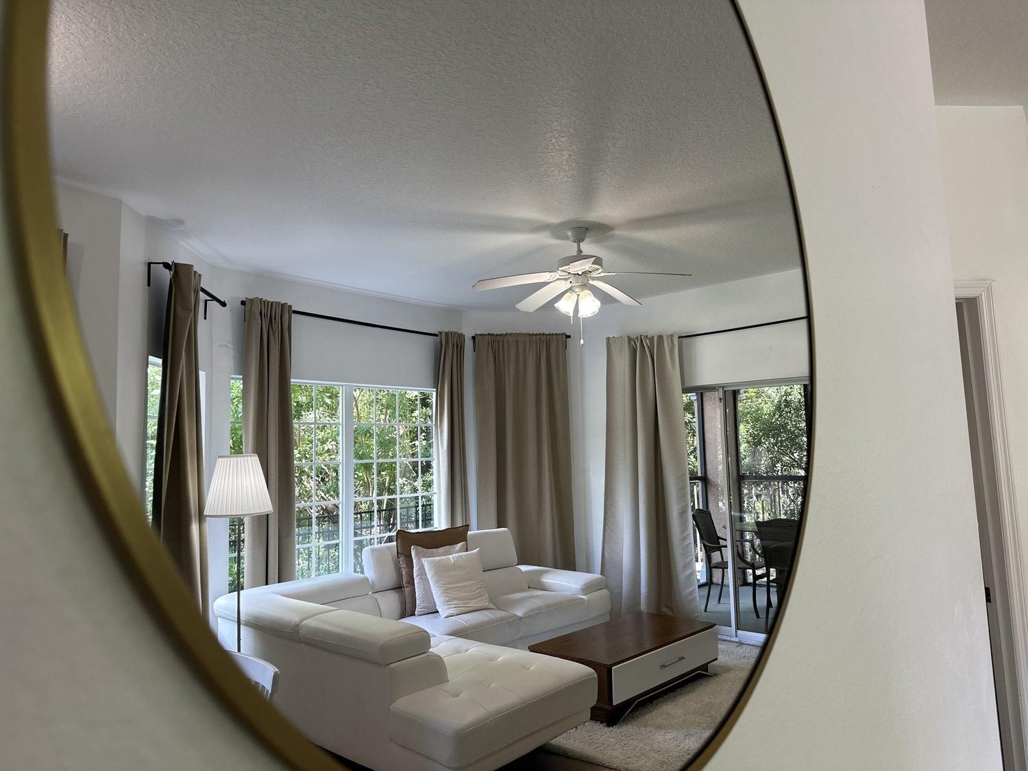 Un salon moderne avec un canapé blanc, un ventilateur de plafond et une vue dégagée sur l’extérieur grâce à une grande fenêtre.