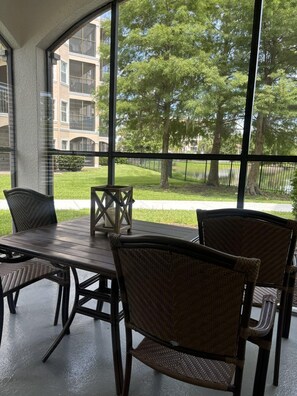 Une terrasse extérieure avec une table et des chaises, de grandes fenêtres offrant une vue sur un quartier résidentiel avec des arbres et une clôture.