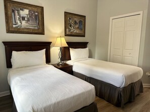 Hotellihuone, jossa on kaksi sänkyä, yöpöytä lampun kanssa ja kaksi kehystettyä kuvaa seinällä.