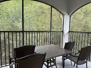 A covered outdoor seating area with a table and chairs, surrounded by a railing, overlooking a dense green landscape. - 4201 Spacious 3/2 Resort Condo Near Disney (Orlando)