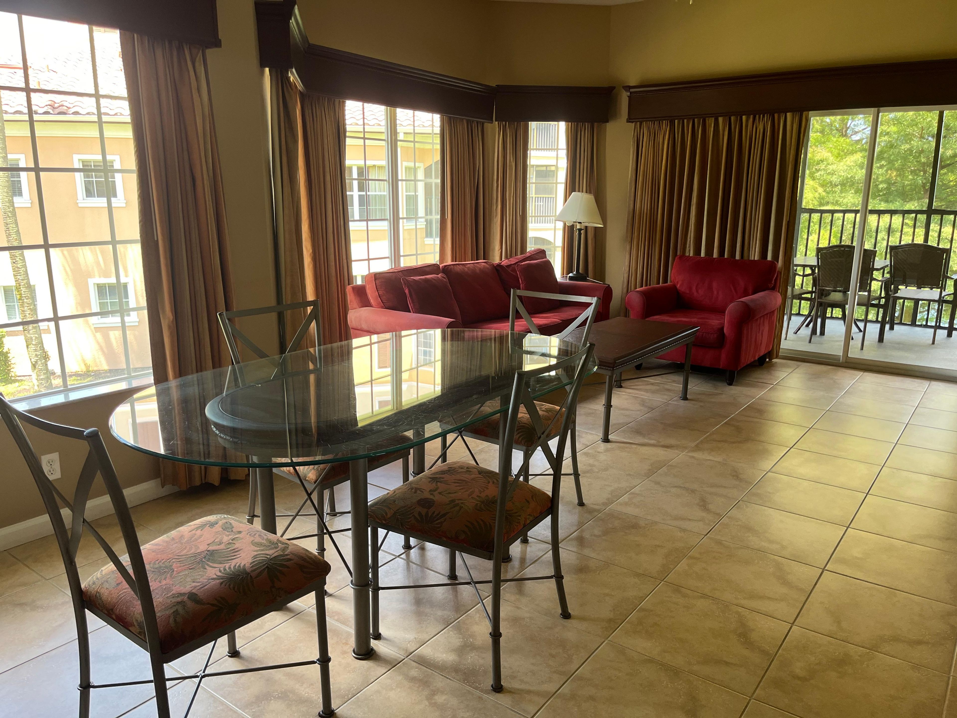 Un salón amplio con mesa de comedor de vidrio, sofás rojos y vista a un balcón.
