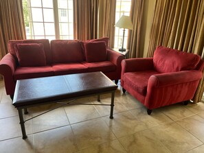 A room with a red sofa, a matching armchair, and a small table. - 4208 Spacious 3/2 Resort Condo Near Disney (Orlando)