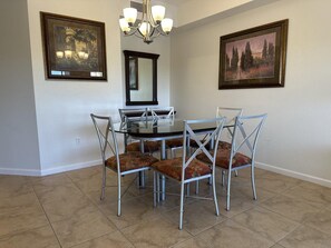 A dining area with a round glass table, metal chairs, a chandelier, and two framed pictures on the walls. - 4307 Spacious 3/2 Resort Condo Near Disney (Orlando)