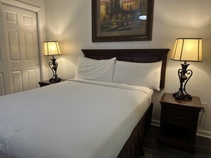 A hotel room with a bed, two bedside tables with lamps, a framed picture on the wall, and a door. - 4307 Spacious 3/2 Resort Condo Near Disney (Orlando)