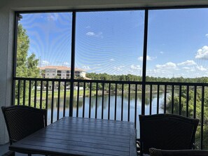 A balcony with a view of a lake, a table, and two chairs. - 4307 Spacious 3/2 Resort Condo Near Disney (Orlando)