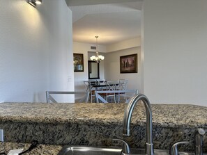 Une cuisine dotée de plans de travail en granit, de robinets en acier inoxydable et d’un coin repas agrémenté d’un lustre.
