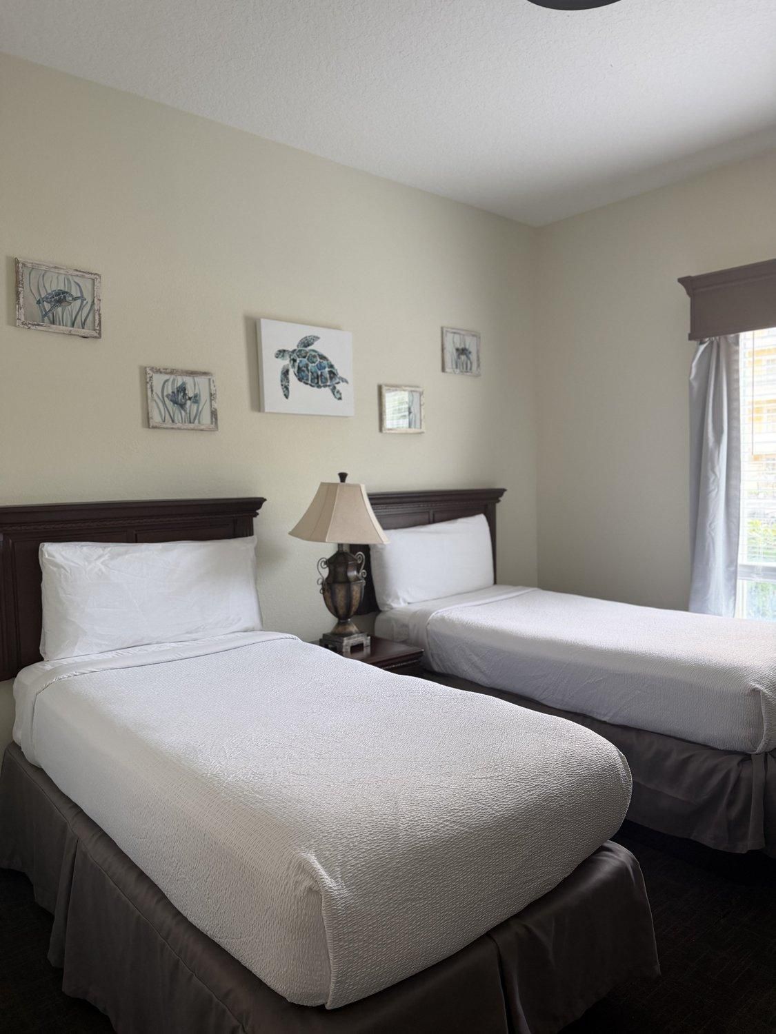 Une chambre d’hôtel avec deux lits, une table de chevet avec une lampe et des œuvres d’art murales.