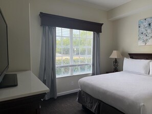 Ein Hotelzimmer mit Bett, Schreibtisch, Lampe und einem Fenster mit Vorhängen.