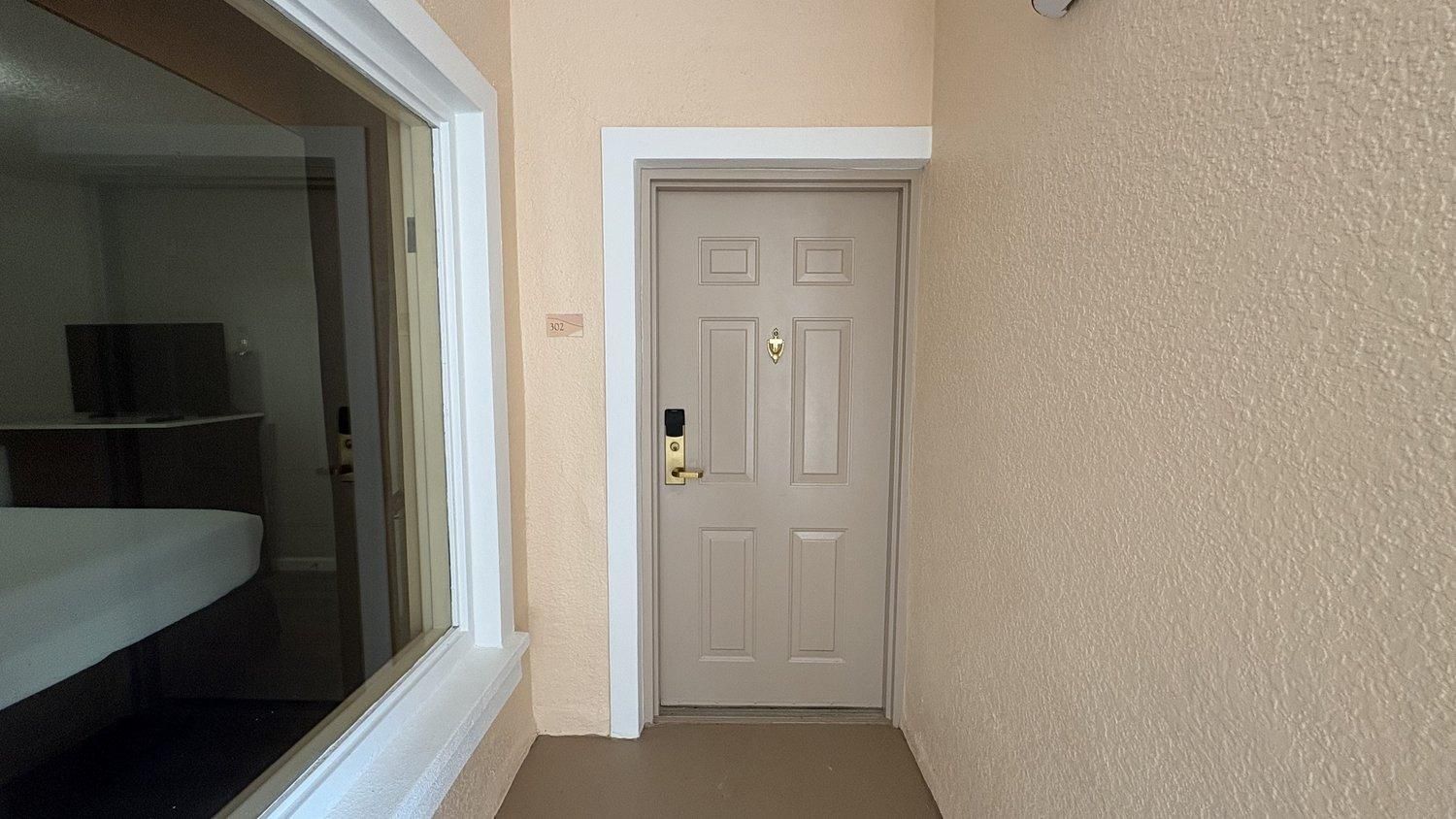 Um corredor com uma porta fechada, uma janela com persianas e uma pequena placa na parede.