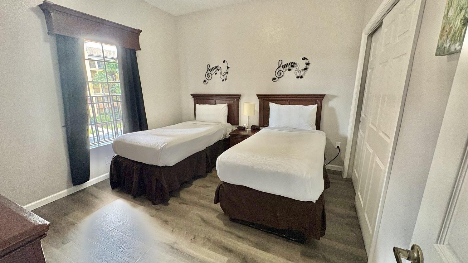 Ein Hotelzimmer mit zwei Einzelbetten, einem Fenster mit Vorhängen und einer Tür.