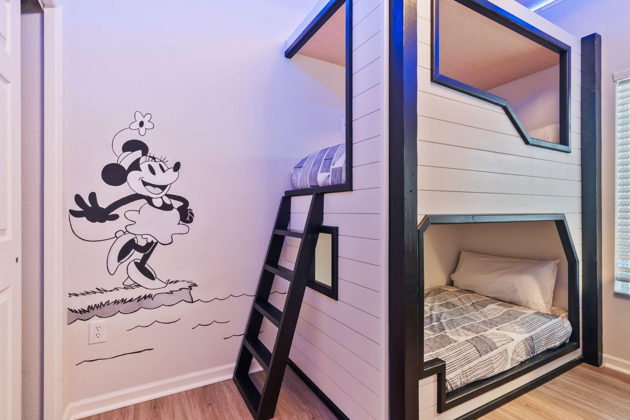 Un lit superposé avec une échelle, un mur décoré d’une fresque représentant Mickey Mouse et une fenêtre avec des stores.