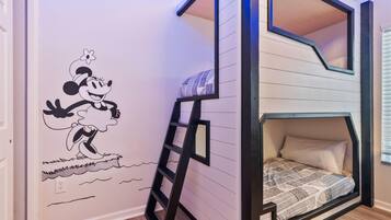 Un lit superposé avec une échelle, un mur décoré d’une fresque représentant Mickey Mouse et une fenêtre avec des stores.