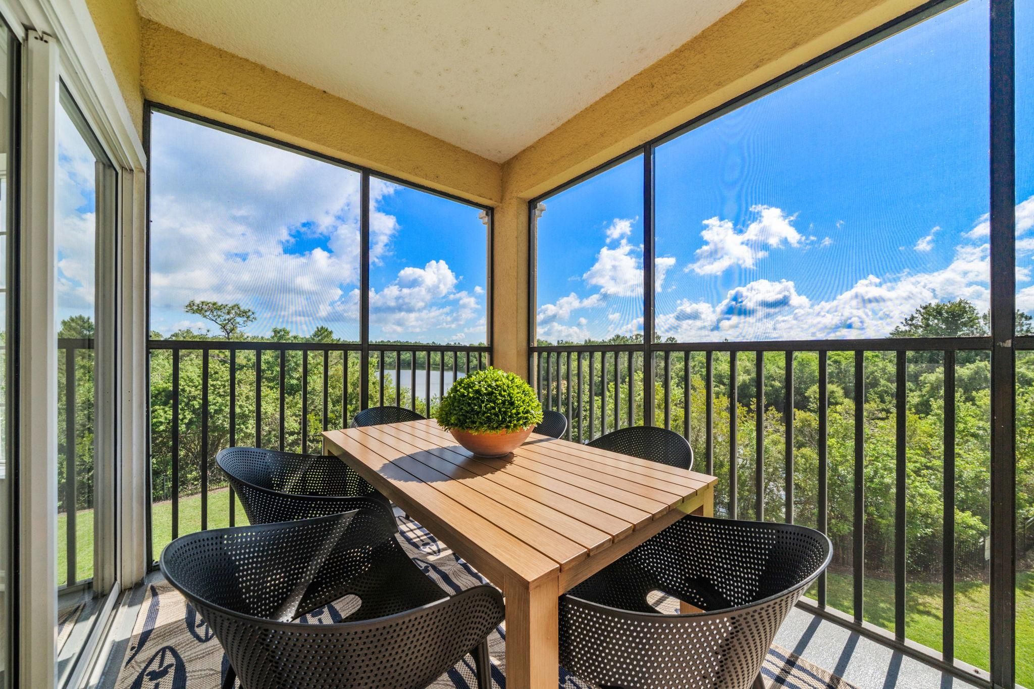 Un balcon abrité avec une table et des chaises en bois, une plante en pot et une vue sur un lac et des arbres.