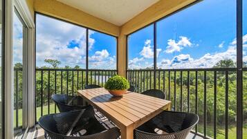 Un balcon abrité avec une table et des chaises en bois, une plante en pot et une vue sur un lac et des arbres.