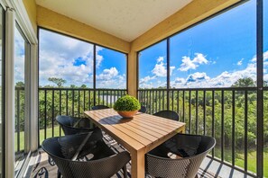 A covered balcony with a wooden table and chairs, a potted plant, and a view of a lake and trees. - 6307 Breathtaking 3/2 Resort Condo Near Disney (Orlando)
