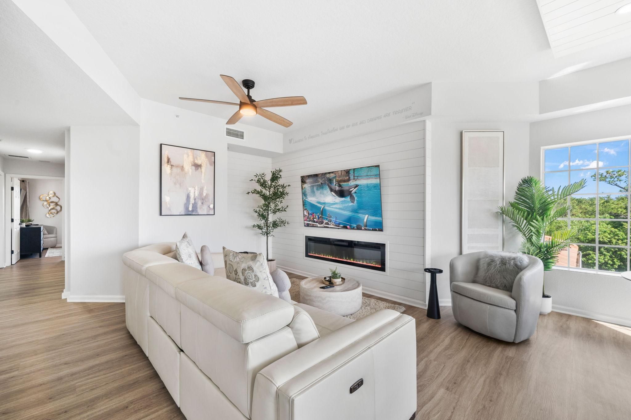 Un salon moderne avec un canapé, un fauteuil et un téléviseur fixé au mur.