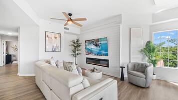 Un salon moderne avec un canapé, un fauteuil et un téléviseur fixé au mur.