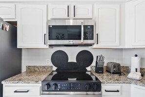 A kitchen with white cabinets, a stainless steel microwave, a gas stove, and a toaster. - 6307 Breathtaking 3/2 Resort Condo Near Disney (Orlando)