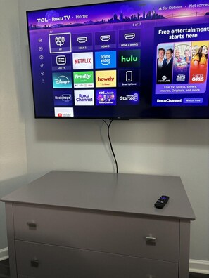 Ein an einer Wand befestigter TCL Roku Fernseher zeigt verschiedene Streaming-Dienste und Kanäle.