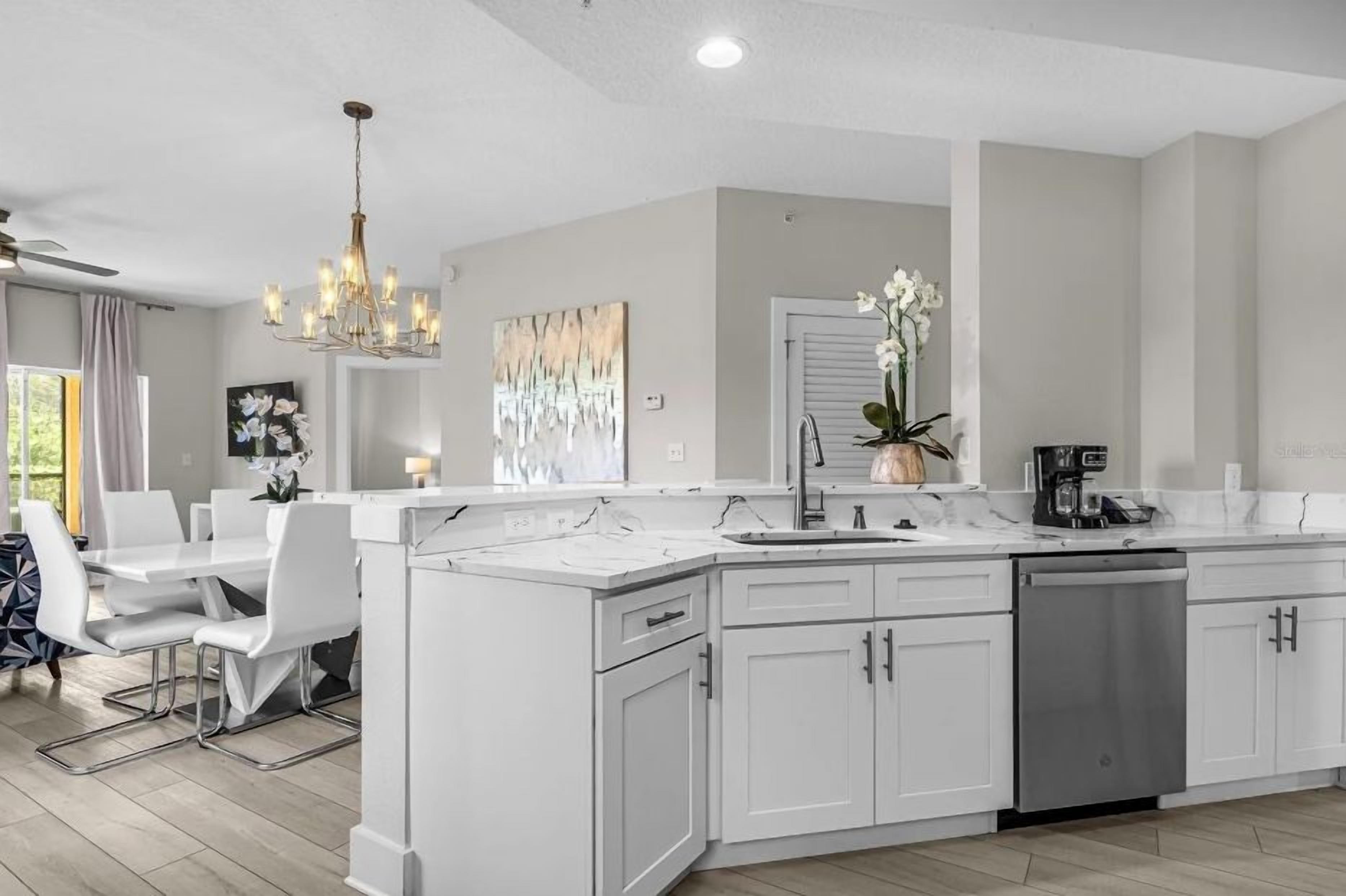 Une cuisine moderne avec des meubles blancs, un îlot central et un coin repas avec des chaises blanches.