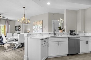 A modern kitchen with white cabinetry, a central island, and a dining area with white chairs.