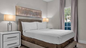 Une chambre d’hôtel avec un lit, deux lampes de chevet, une table de chevet avec des tiroirs, une fenêtre avec des rideaux et un tableau au mur.