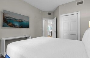 A bedroom with a bed, a painting, a white door, and a hallway leading to a bathroom. - 6204 Luxurious 3/3 Resort Condo Near Disney (Orlando)