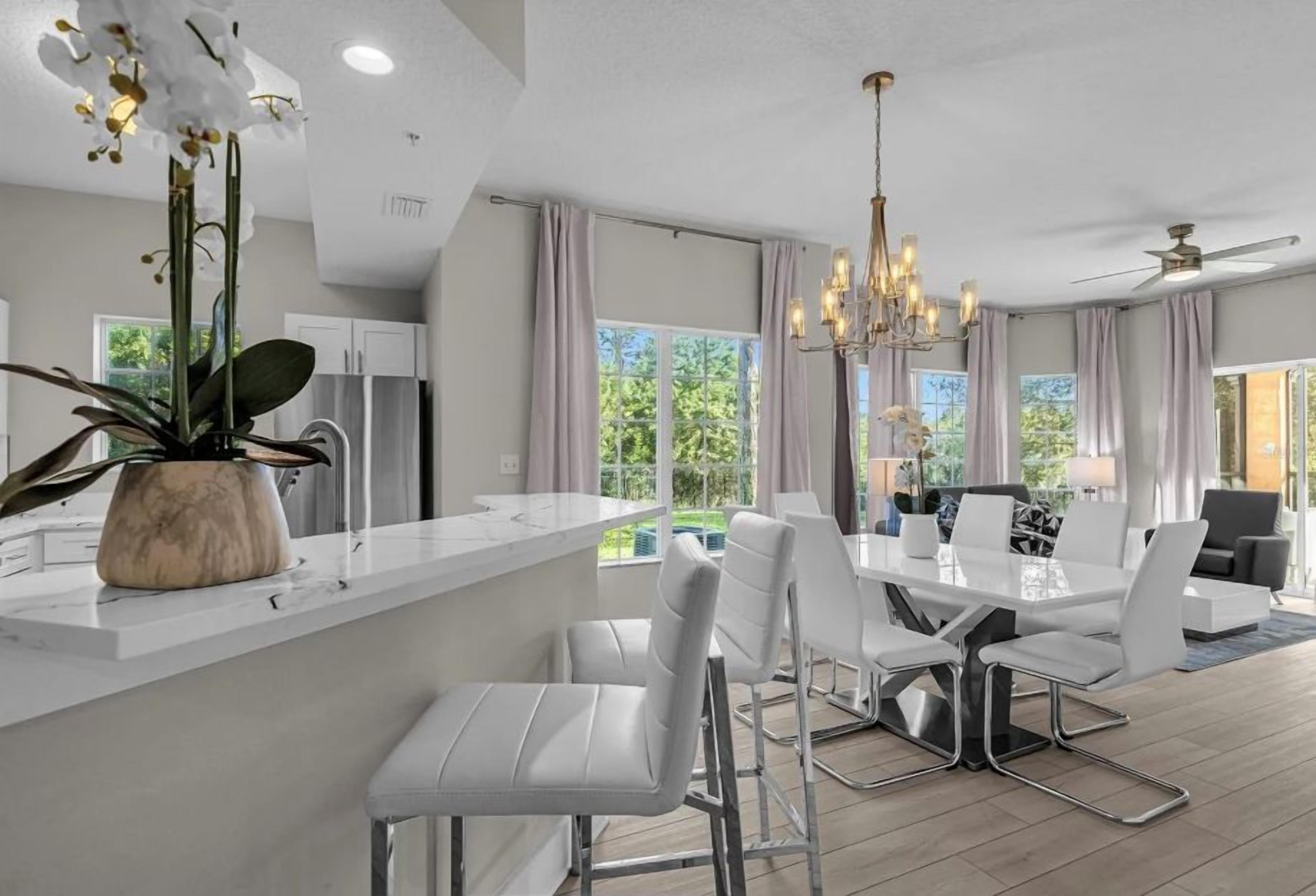 A modern kitchen with a white countertop, a dining area with white chairs, and a chandelier.