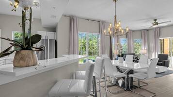A modern kitchen with a white countertop, a dining area with white chairs, and a chandelier.