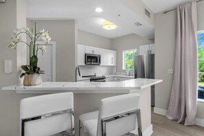 A modern kitchen with white cabinetry, a central island, and stainless steel appliances. - 6204 Luxurious 3/3 Resort Condo Near Disney (Orlando)