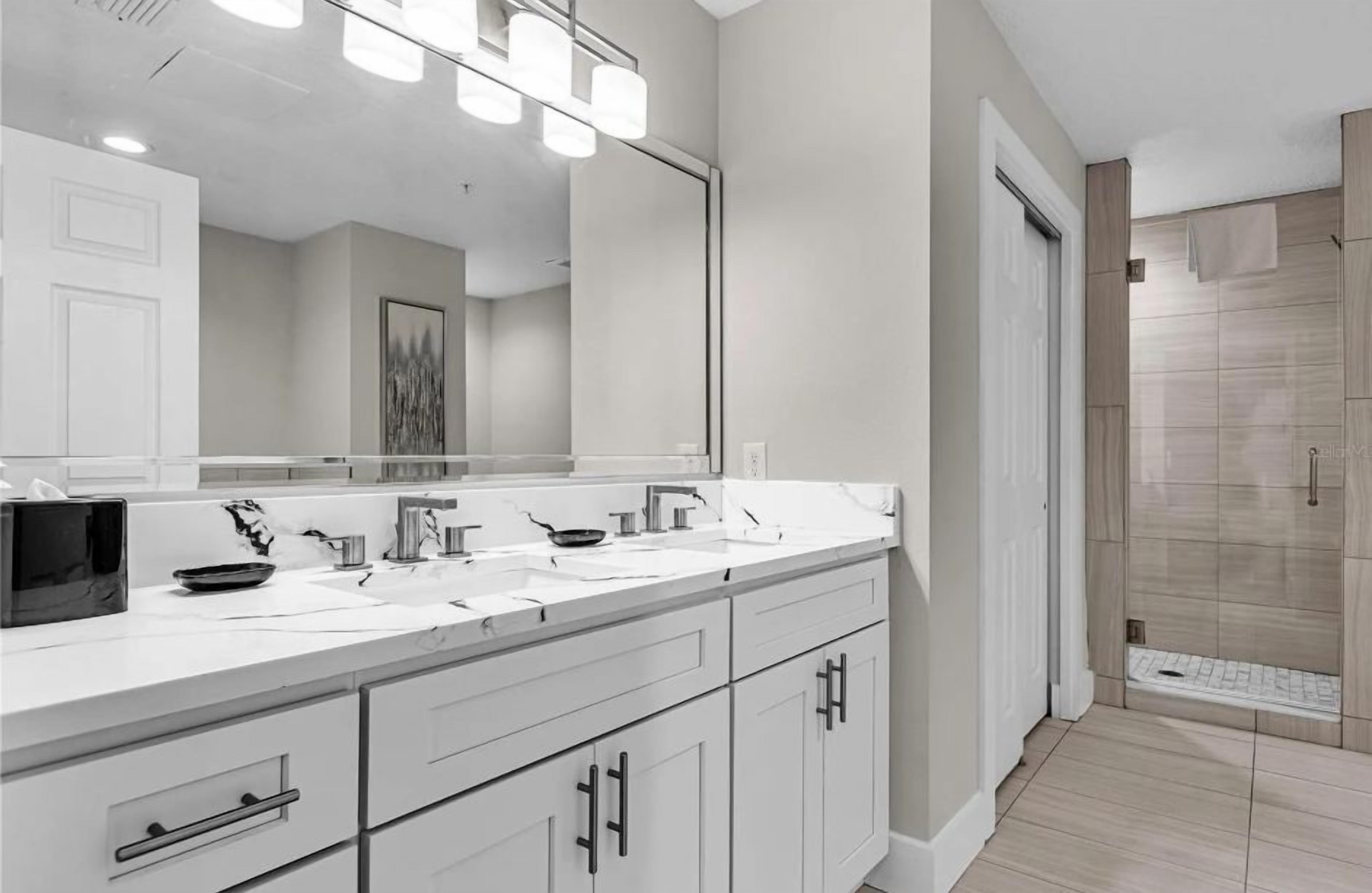 Une salle de bain moderne avec un meuble-lavabo à deux vasques, un grand miroir et une douche à l’italienne.