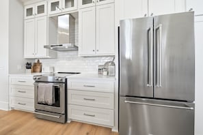 A modern kitchen with white cabinetry, a stainless steel refrigerator, and a built-in oven. - Oceanfront Jekyll Island • 3 King Bedrooms • Screened Porch • Walk to Dining (Jekyll Island)