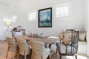 A dining area with a wooden table, wicker chairs, and a painting above. - Oceanfront Jekyll Island • 3 King Bedrooms • Screened Porch • Walk to Dining (Jekyll Island)
