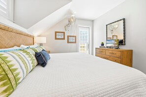 Quarto com cama grande, cabeceira de madeira, cômoda, espelho e obras de arte nas paredes.