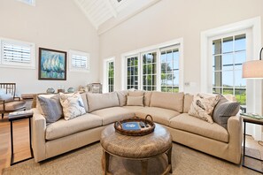 A spacious living room with a large L-shaped sectional sofa, a round coffee table, and a painting on the wall. - Oceanfront Jekyll Island • 3 King Bedrooms • Screened Porch • Walk to Dining (Jekyll Island)