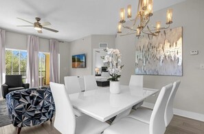 Een eetgedeelte met een witte tafel, witte stoelen, een plafondventilator en een kroonluchter.
