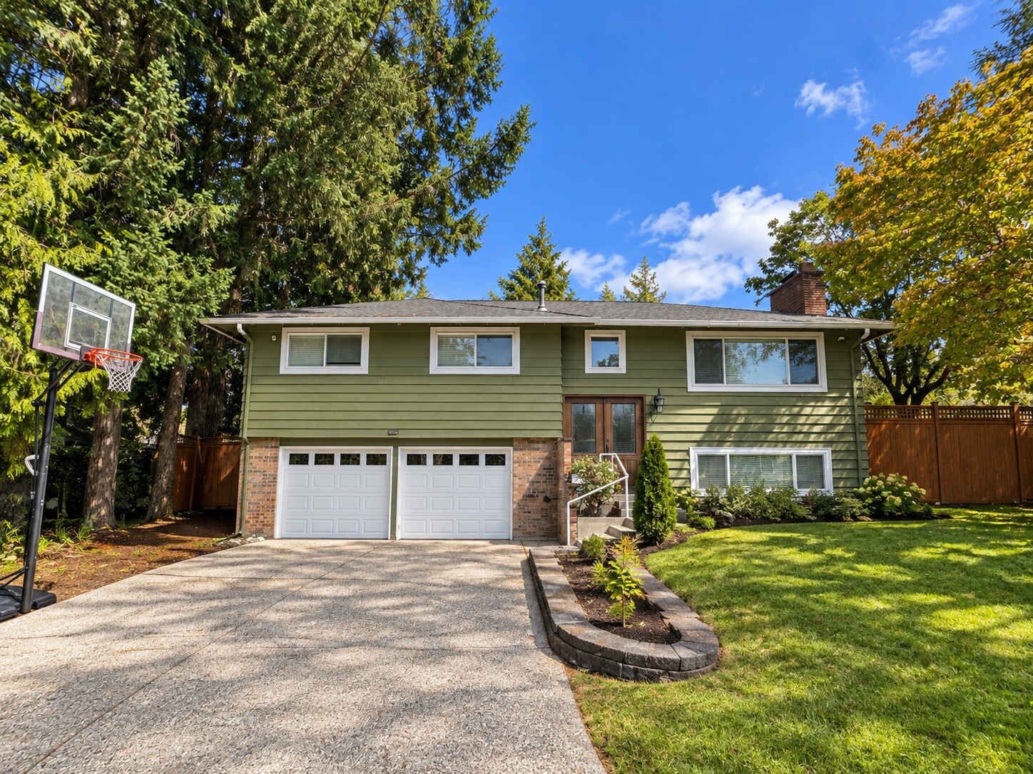 A two-story house with a garage, a basketball hoop, and a well-maintained lawn.