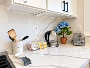 Een keuken met witte kasten, een marmeren aanrecht, een koffiezetapparaat, een broodrooster, een plant en diverse keukengerei.