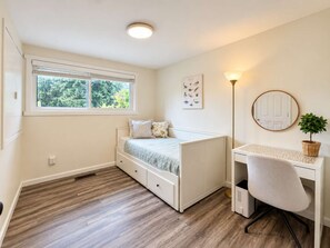 Een slaapkamer met een bed, een bureau, een stoel, een radiator, een raam en een plant.