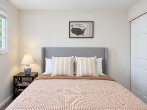 Ein Schlafzimmer mit einem Bett, einem Nachttisch mit Lampe, einer gerahmten Karte an der Wand und einer Tür.