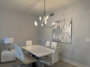 Ein Essbereich mit einem weißen Tisch, vier Stühlen, einer Chandelierleuchtre und einem Gemälde an der Wand.