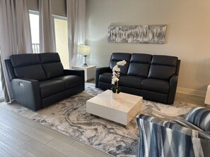 A modern living room with two black leather sofas, a white coffee table, and a patterned rug. - 6304 Luxurious 3/3 Resort Condo Near Disney (Orlando)
