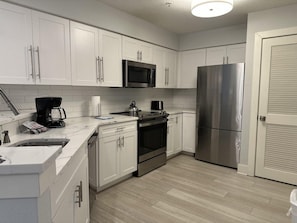 A modern kitchen with white cabinets, stainless steel appliances, and a tiled backsplash. - 7205 Luxurious 3/3 Resort Condo Near Disney (Orlando)