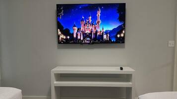 Une chambre à coucher avec un téléviseur fixé au mur, diffusant une scène de château, une console blanche et deux lits.