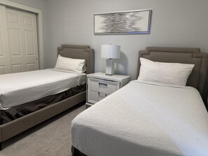 A hotel room with two beds, a nightstand, a lamp, and a framed picture on the wall.