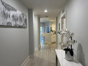 A hallway with a white bench, a white vase with flowers, and a painting on the wall.