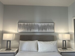 A bedroom with a bed, two bedside lamps, and a large abstract painting on the wall.