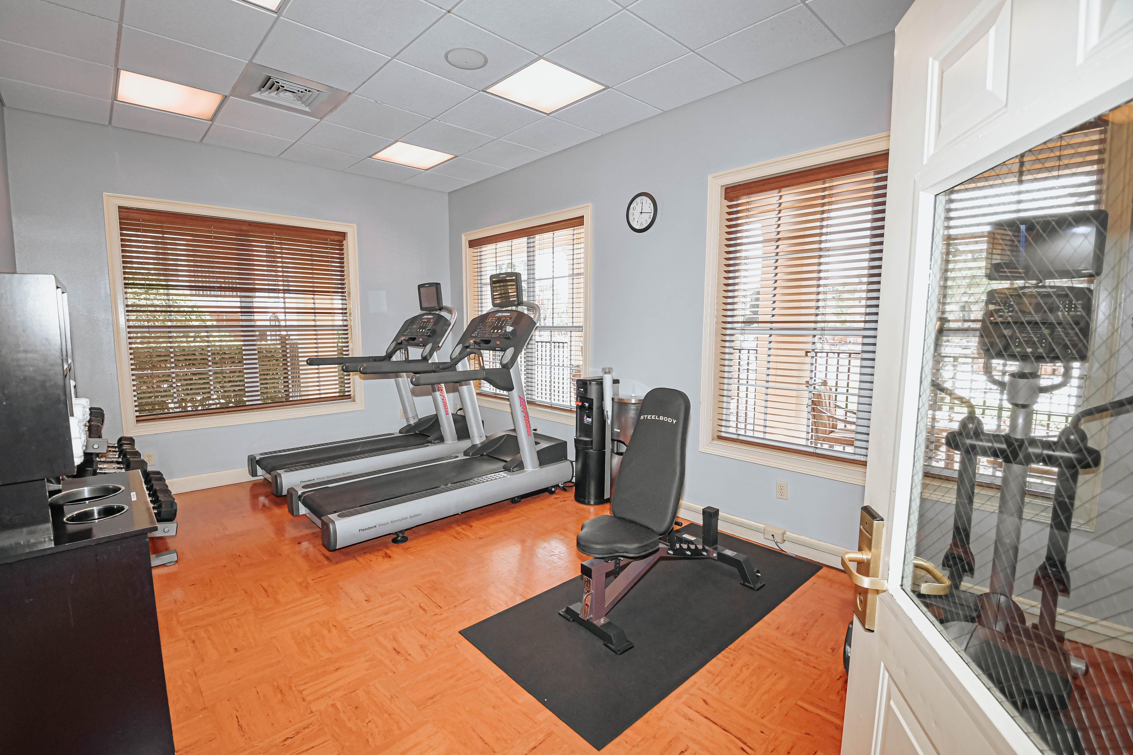 Une salle de sport équipée de tapis de course, d’un banc de musculation et d’une horloge murale.