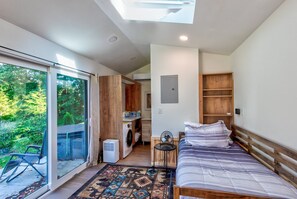 A bedroom with a bed, a fan, a washing machine, and a view of greenery through a sliding door. - Glamping Pods at Tiffany's Estate | Hot Tub, Fire Pit, Pickleball, & Pond (Elk Park)